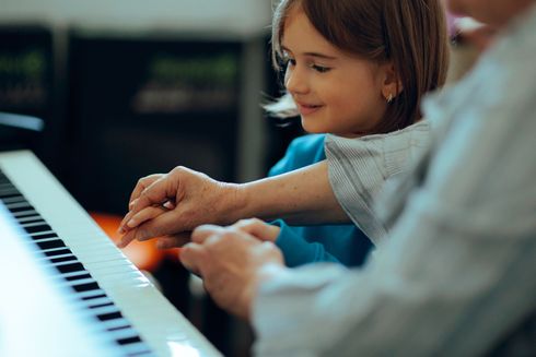 Child and adult playing piano together, hands on keys, smiling in a bright room