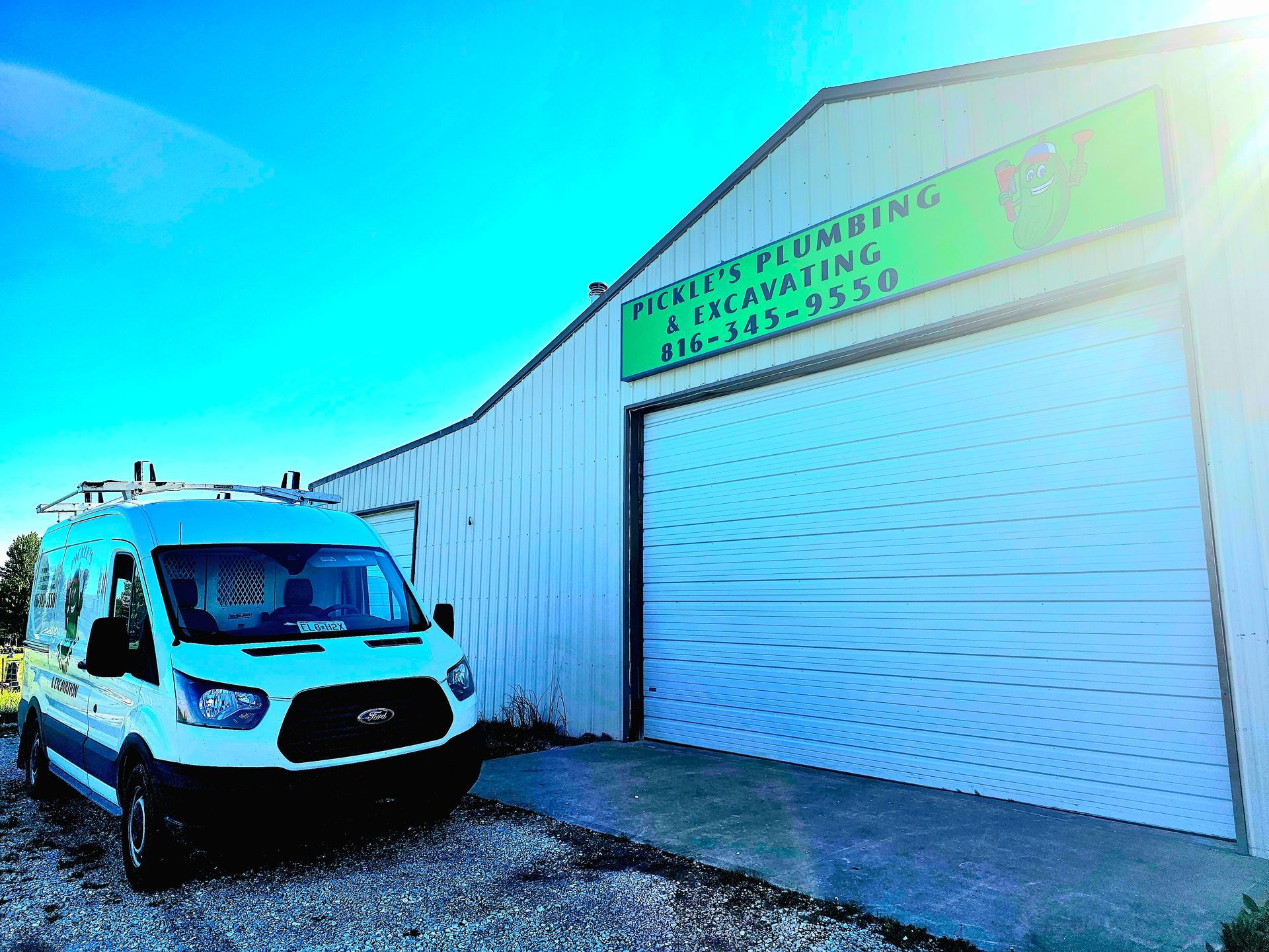 White work van parked beside a metal garage with a green business sign above the door.