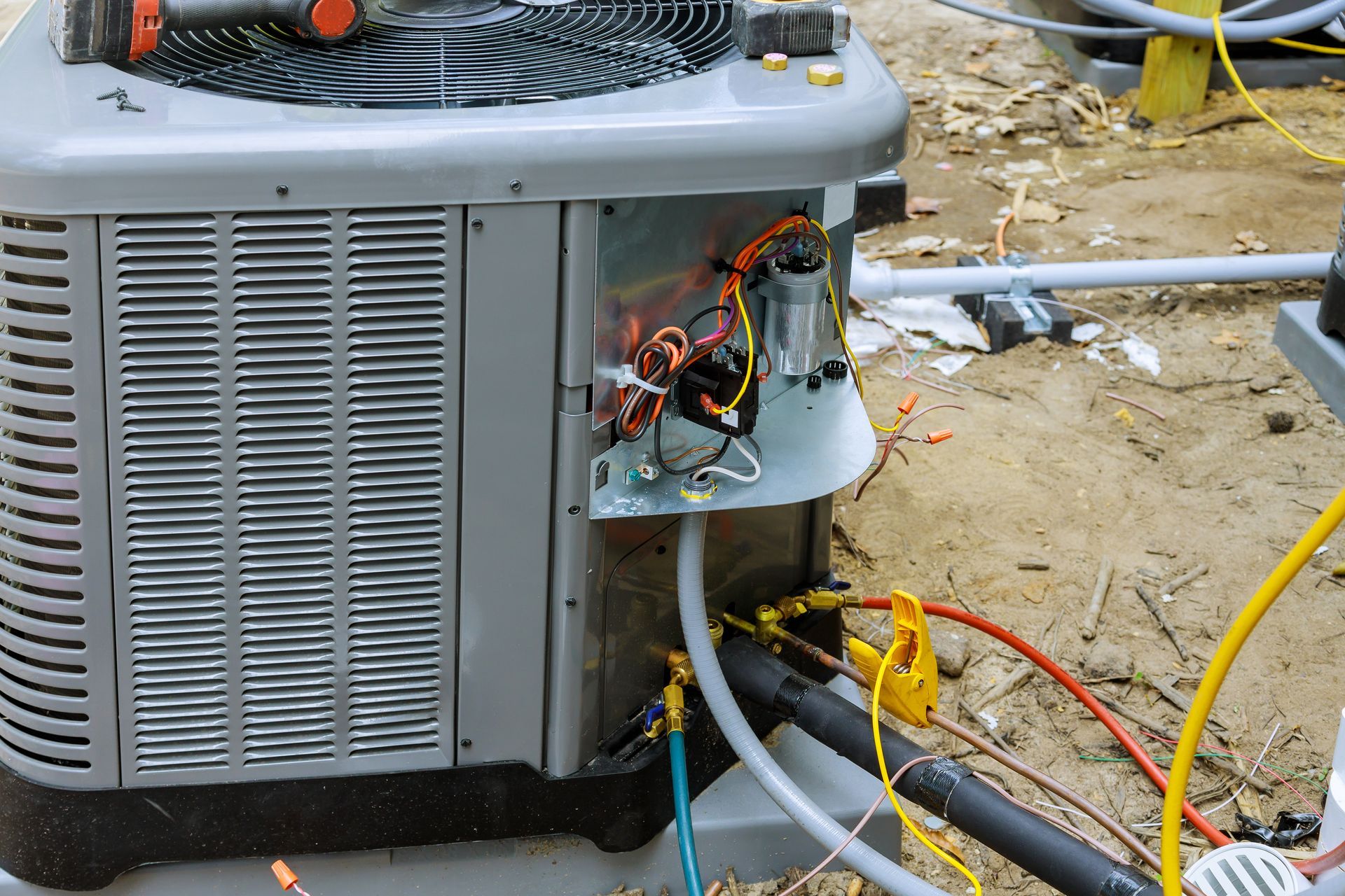 An outdoor air conditioning unit with its service panel removed, revealing internal wiring and attached gauge hoses.