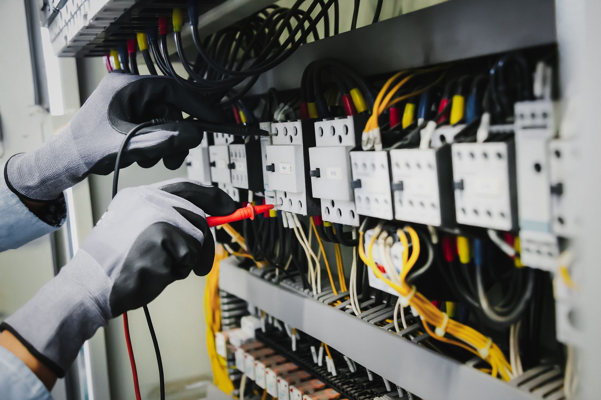 Electrician testing wires in a control panel, wearing gloves.