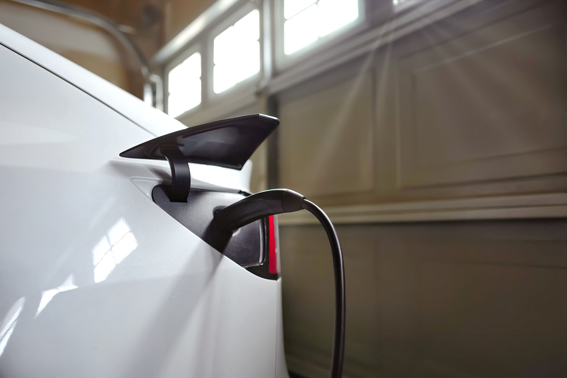 White electric car charging in a garage; charging cable plugged into the car.