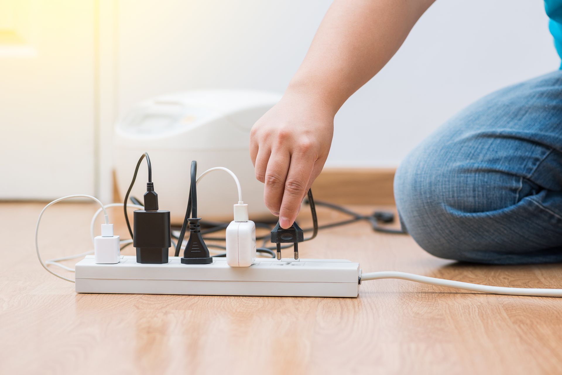 Person plugging a power cord into an overloaded power strip on a wooden floor.