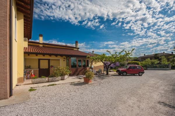 Cortile con edifici in mattoni, parcheggio ghiaioso e un'auto rossa sotto un cielo blu