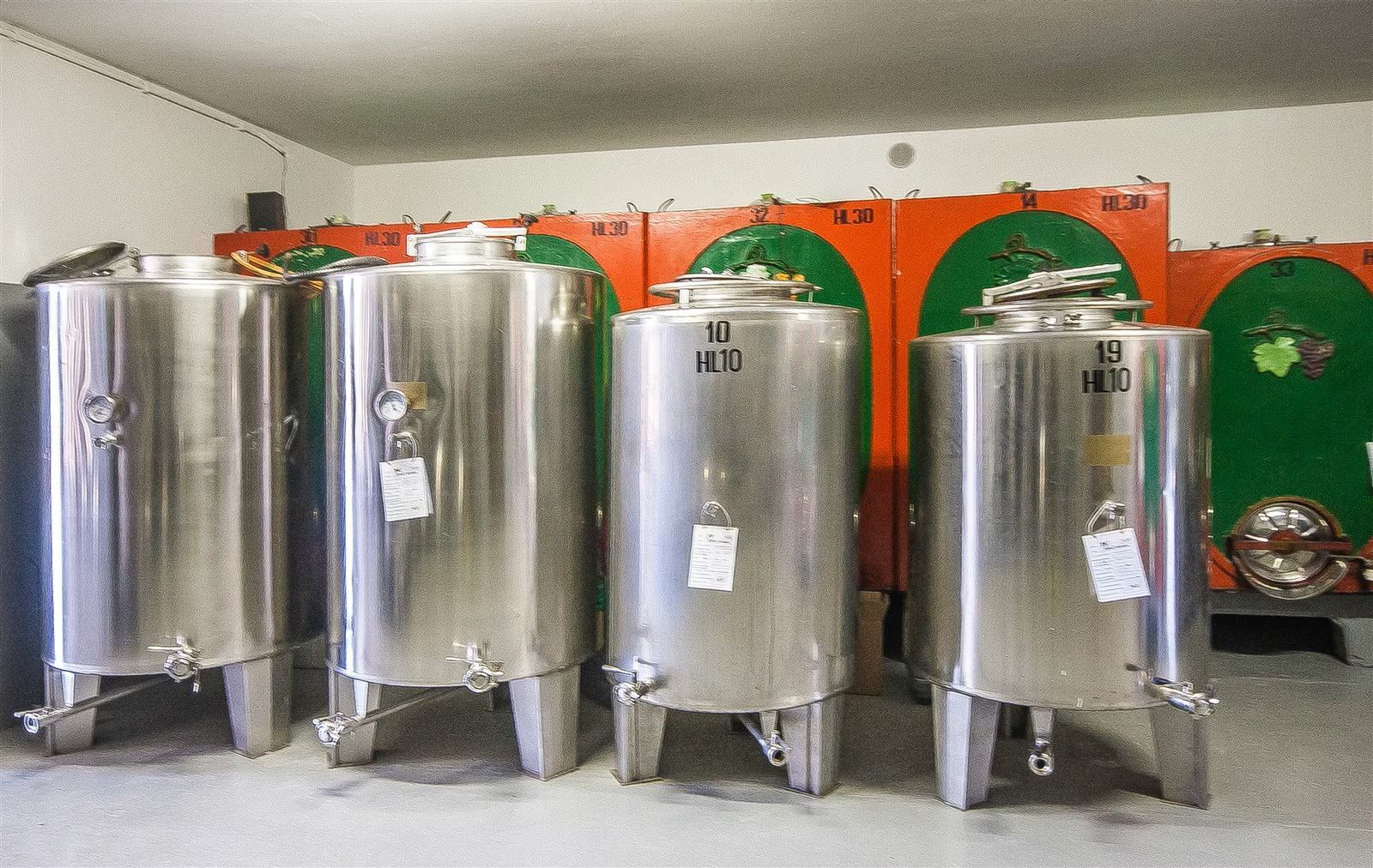 Una fila di serbatoi in acciaio inox in un locale industriale con pannelli a parete arancioni e verdi.
