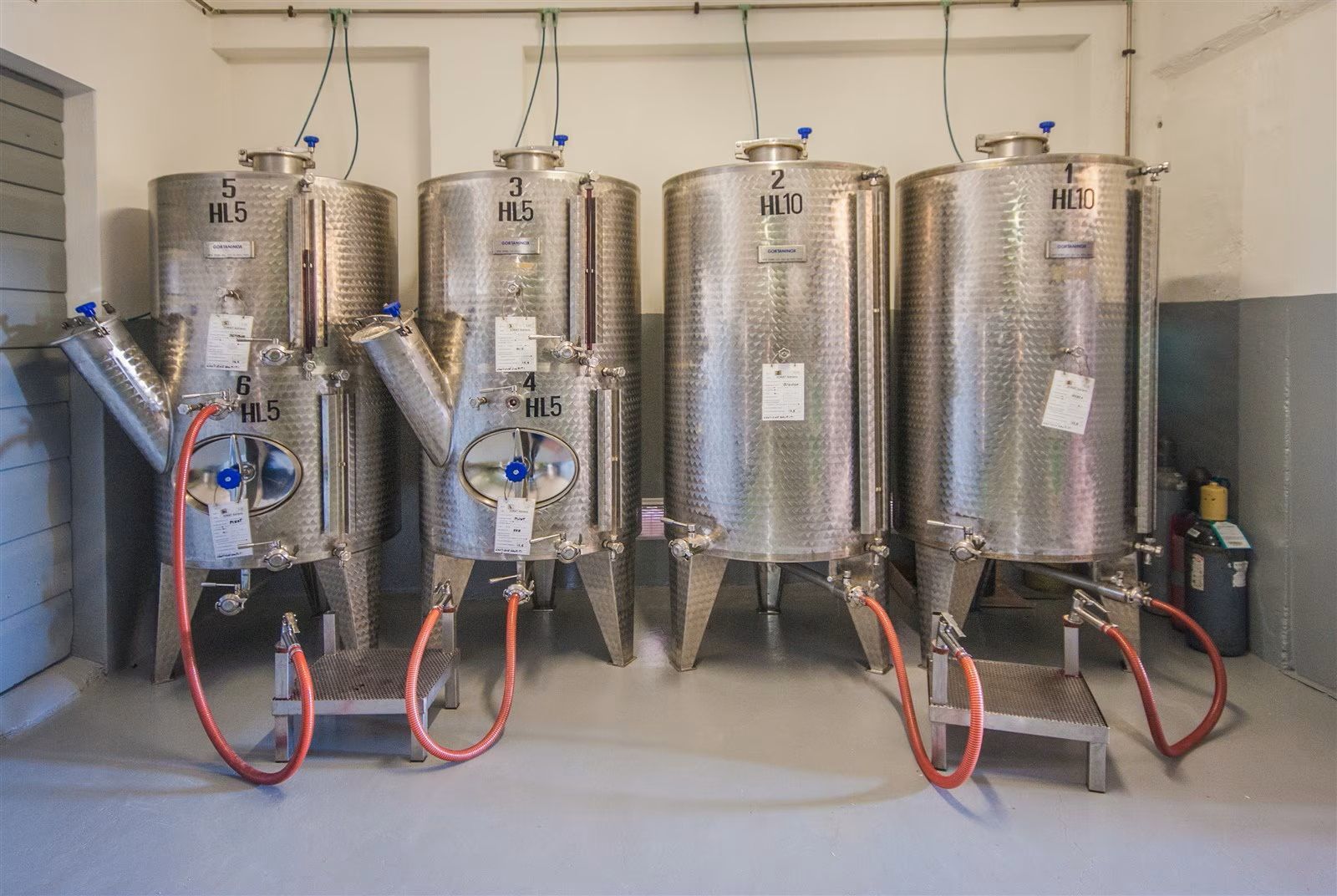 Quattro serbatoi di birra in acciaio inox con tubi flessibili in un locale industriale.