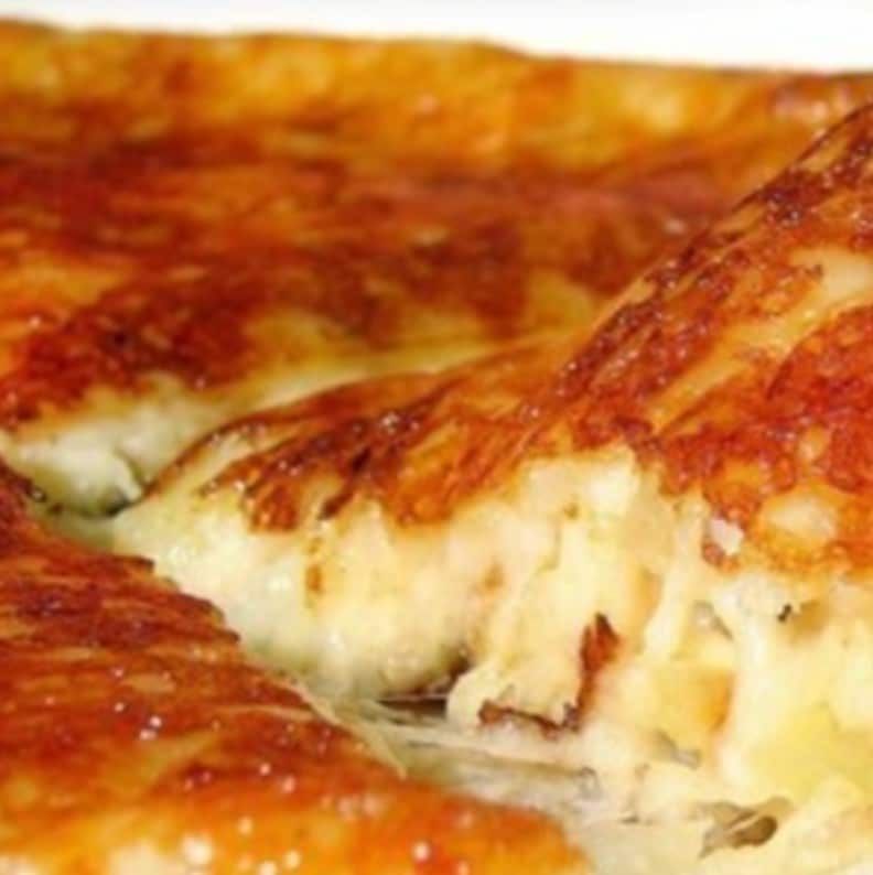 Primo piano di una fetta di pizza al formaggio dorata con formaggio fuso e crosta croccante.