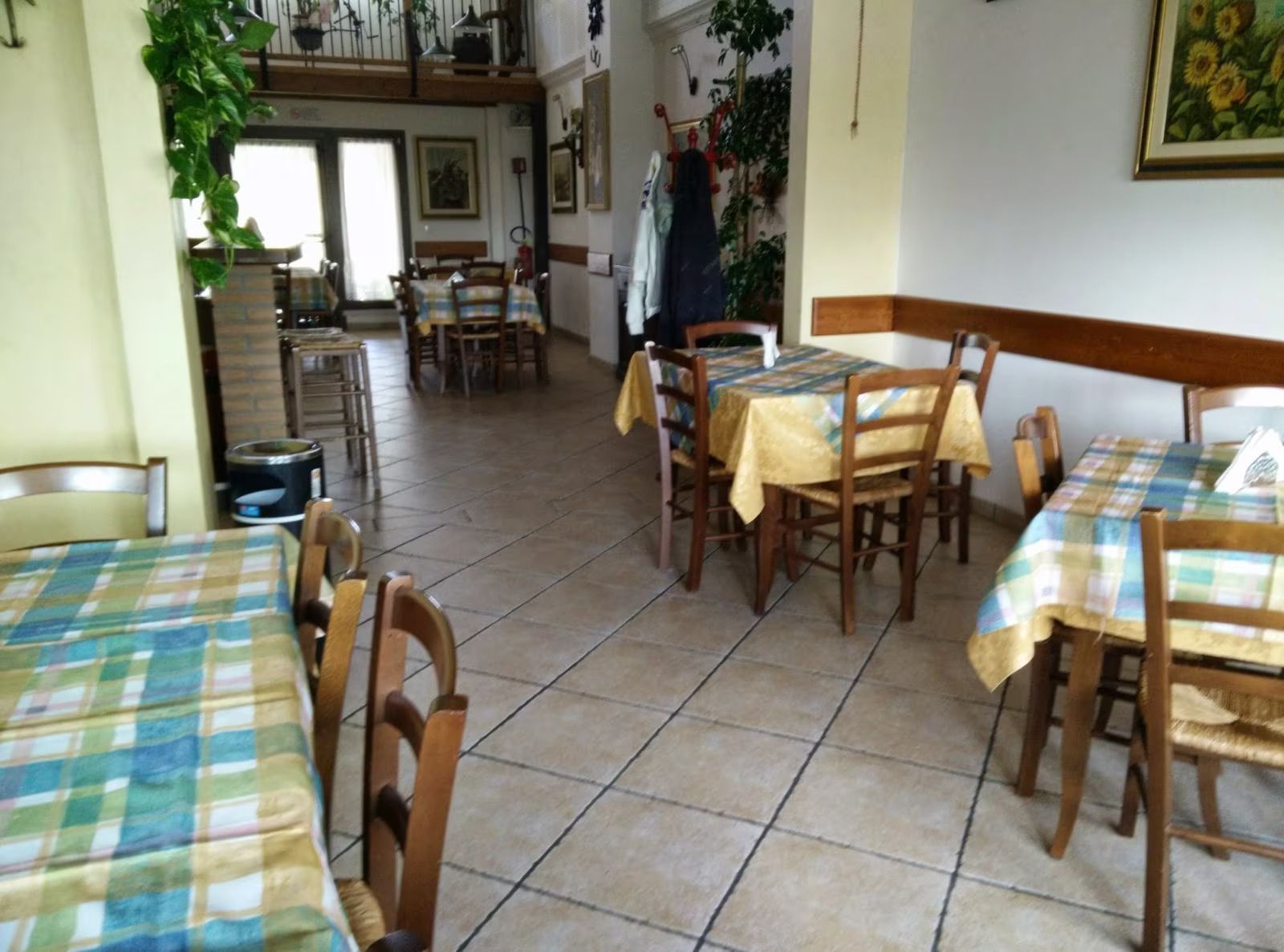 Accogliente sala da pranzo di un ristorante con tovaglie a quadri, sedie in legno e pavimento piastrellato.