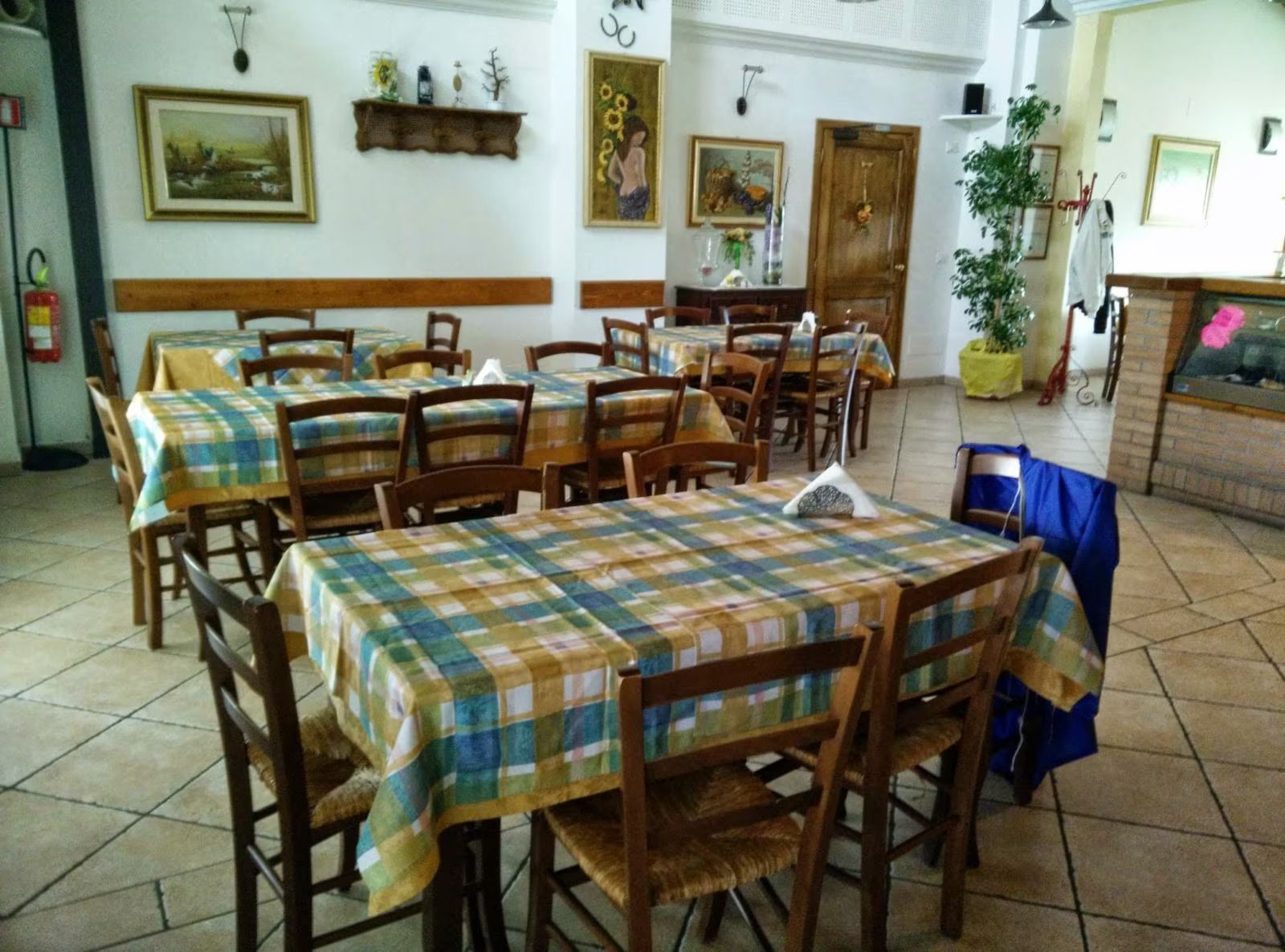 Sala da pranzo rustica vuota con tovaglie a quadri, sedie di legno, decorazioni alle pareti e pavimento piastrellato.
