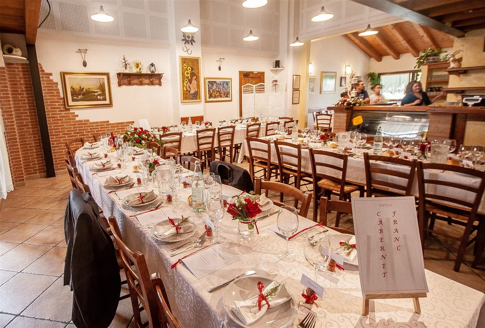 Lungo tavolo da banchetto allestito per pranzare in un ristorante rustico con sedie e pareti in mattoni.