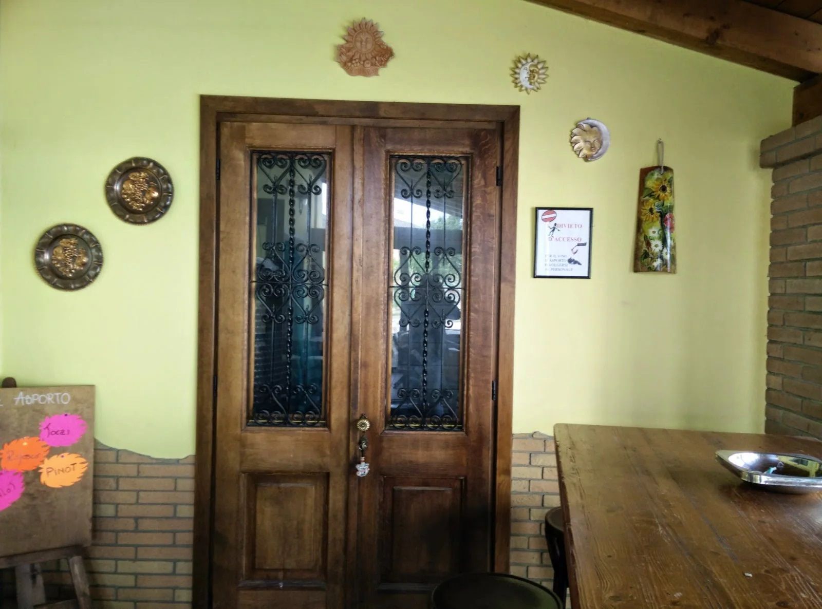 Doppia porta d'ingresso in legno su una parete gialla, fiancheggiata da piatti decorativi e un tavolino.
