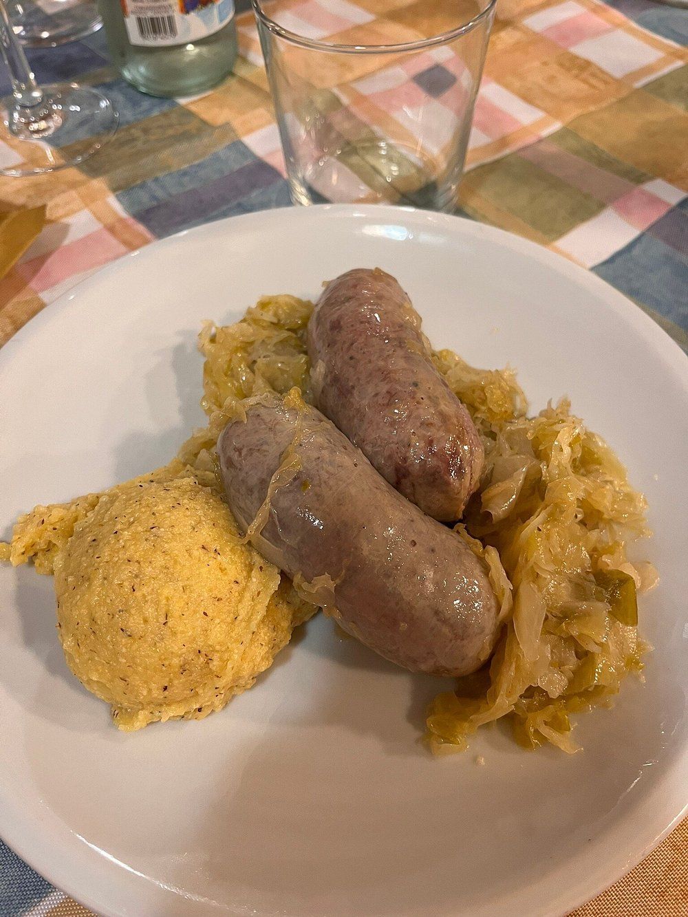 Piatto con due salsicce, crauti e una fetta di pane di mais su una tovaglia.