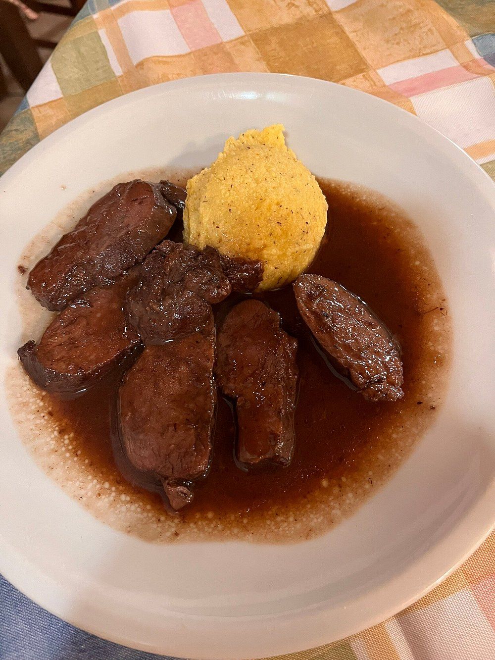Piatto di salsicce marrone scuro con una porzione di purè di patate giallo e salsa gravy marrone su una tovaglia a quadri.