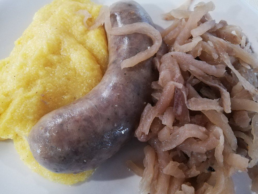 Piatto con contorno di purè di patate giallo, salsiccia e cipolle saltate.