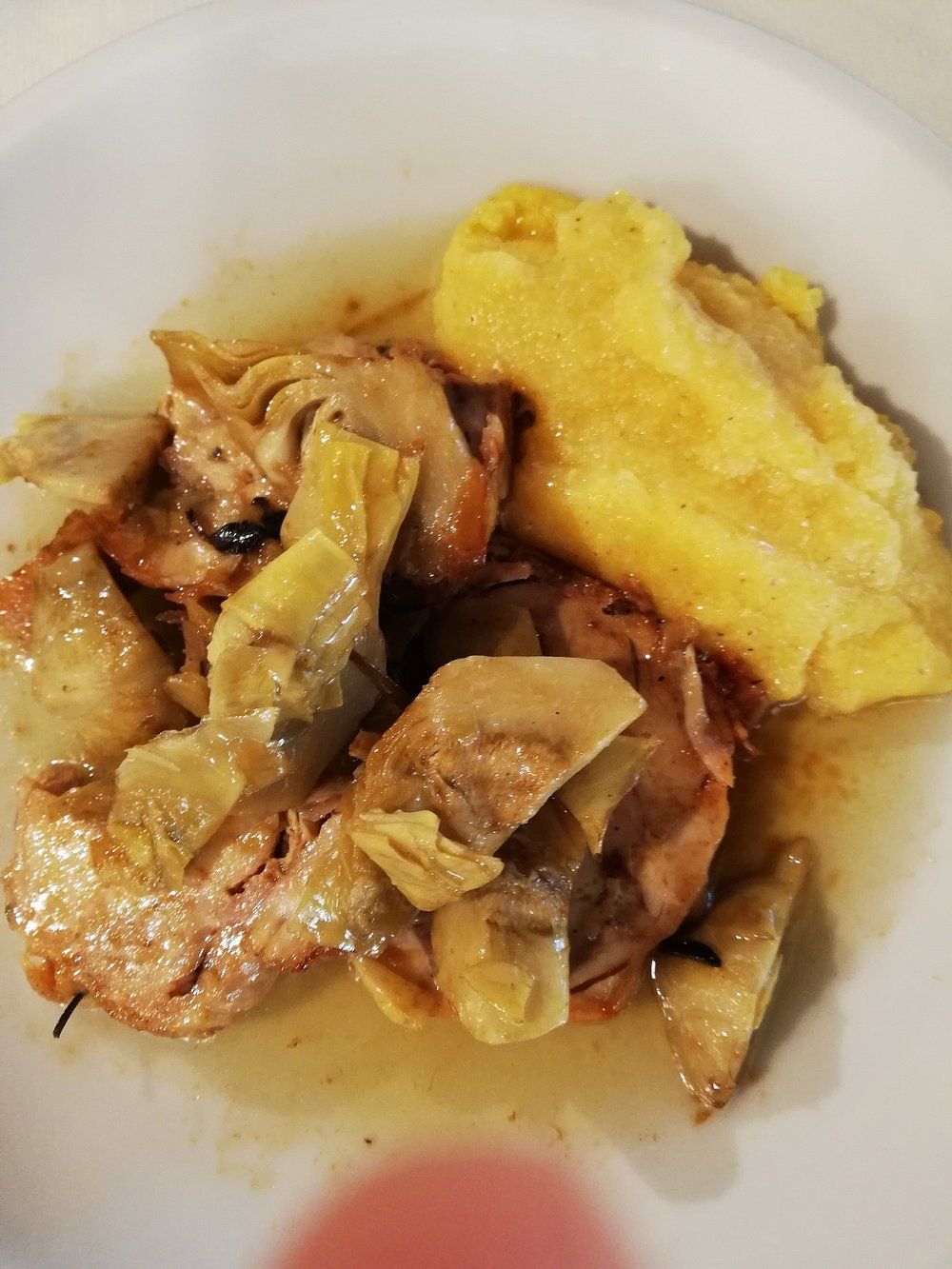 Un piatto di pollo cotto e verdure con una frittata gialla o polenta su un piatto bianco.