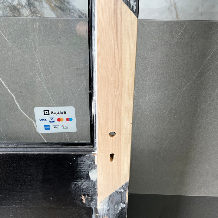 Close-up of a door frame with visible lock holes, partially painted black, with a Square sticker.
