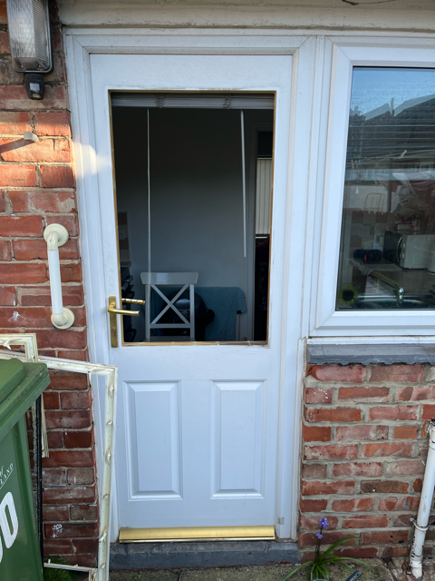 White back door with open upper panel, showing a small chair inside, beside brick wall and window.