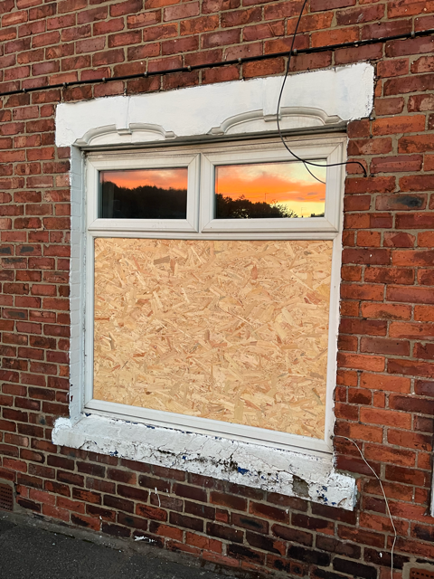 Boarded-up white-framed window in a brick wall at sunset.