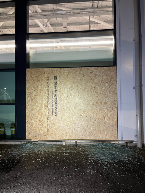 Boarded-up storefront with plywood over a glass window and a dark sidewalk at night