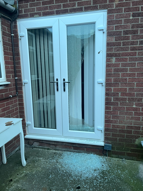 White double patio doors on a brick house with vertical blinds, beside a small table and wet concrete.