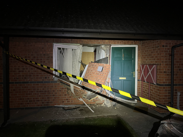 Destroyed doorway at night with fallen debris and police tape across a brick building