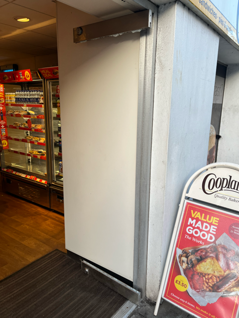 Store entrance with a wide open doorway, white wall, and Co-op Value Made Good sign on the right.