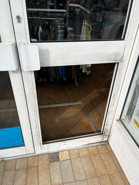 Store entrance with glass door open over a threshold and tiled sidewalk outside