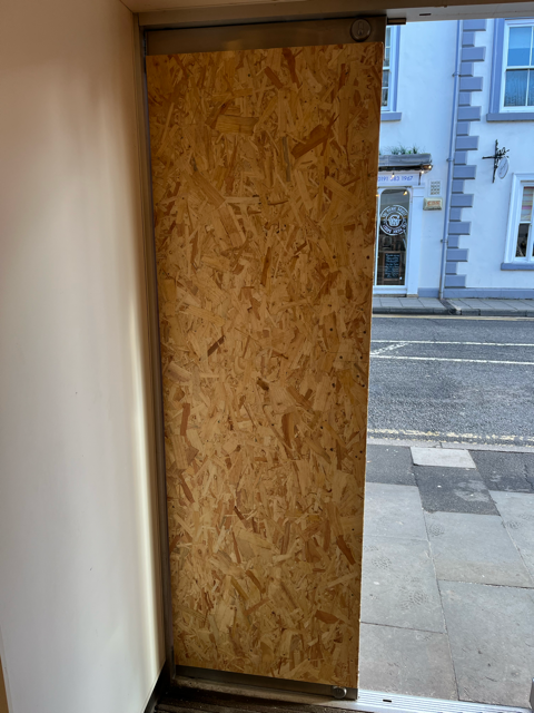 Boarded-up doorway from inside, looking out to a street and sidewalk.