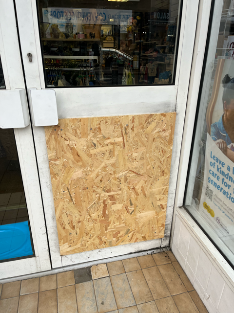 Boarded-up storefront door with plywood panel over the lower glass and tiled entrance floor