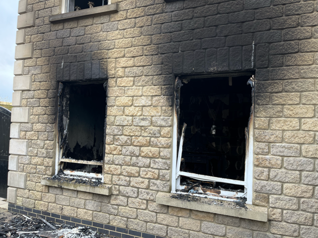 Soot-covered stone building with two burned-out windows and damaged white frames