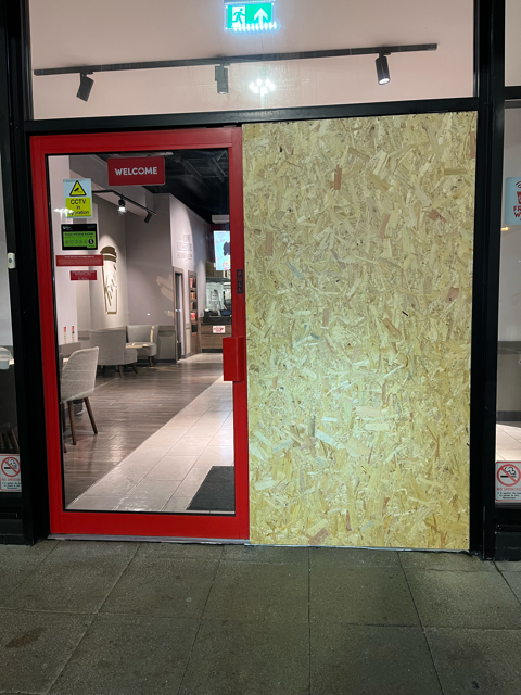 Red doorway into a hallway with gray flooring and a lit exit sign above.