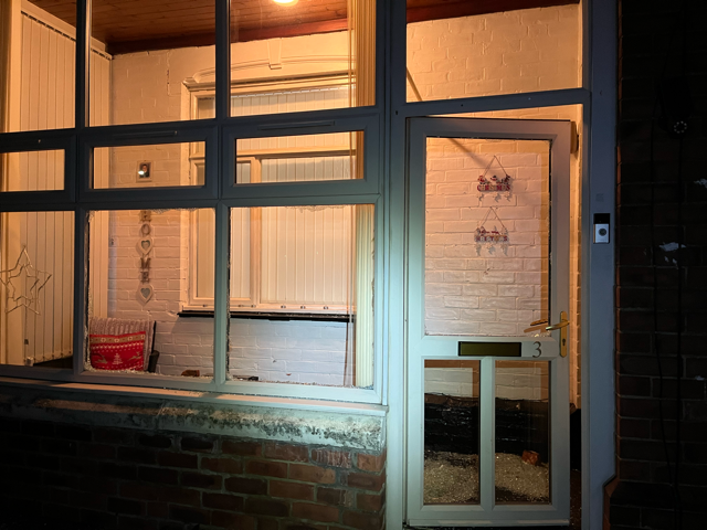 Storefront window and door at night, warmly lit with blinds and a small red chair inside.
