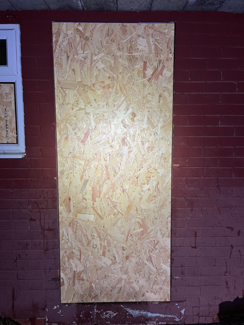 Plywood board covering a window opening on a red brick wall at night