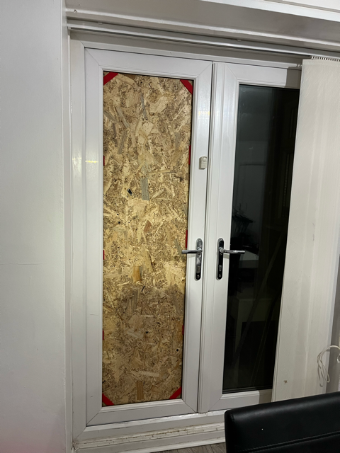 Boarded-up window beside a white French door with dark glass panel