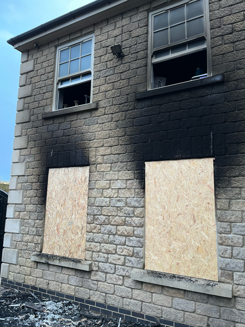 Soot-blackened brick building with boarded windows after a fire