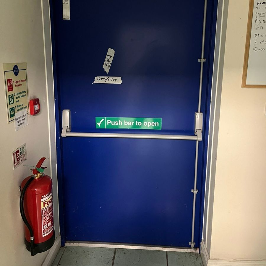 Blue fire exit door with a push bar, fire extinguisher, and safety signs.
