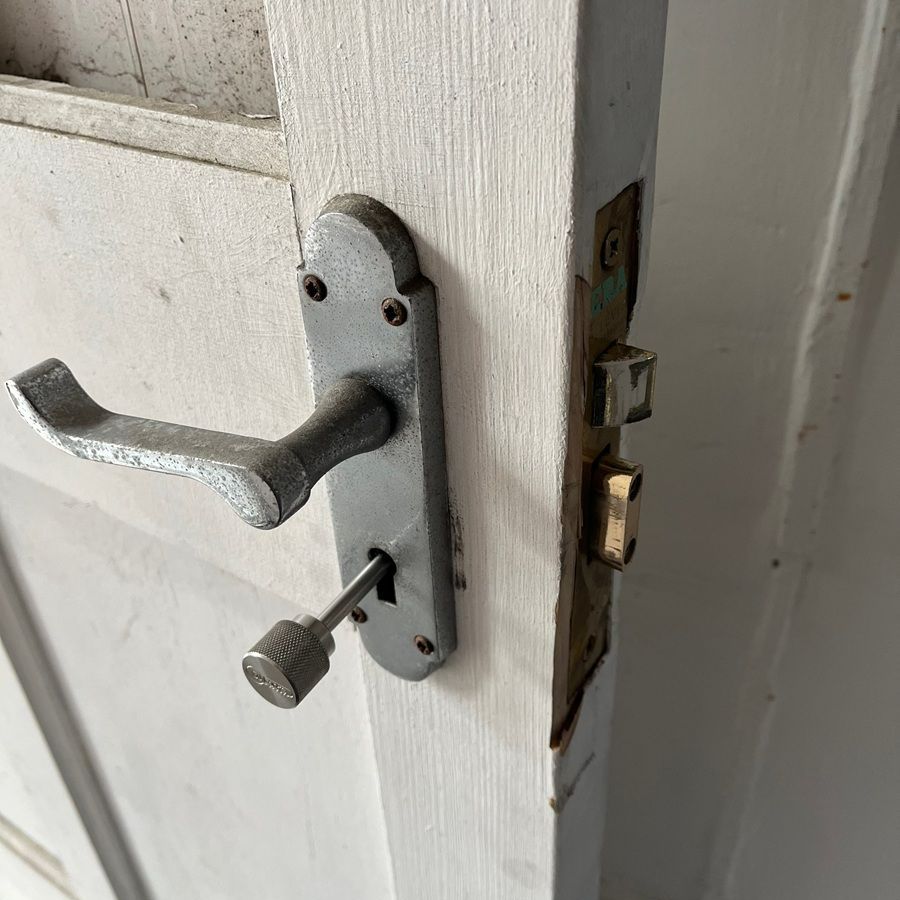 Silver door handle with a key, mounted on a white door. The door frame has a strike plate.