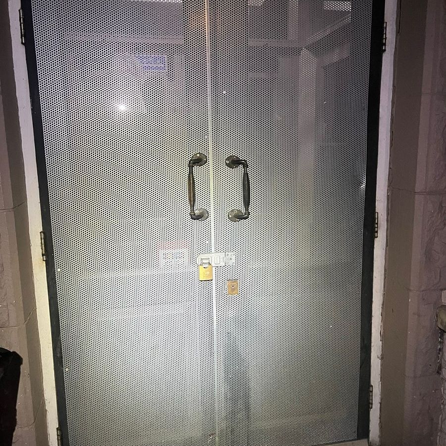 Metal security doors, double-paned with a diamond pattern, locked with padlocks, outdoors.