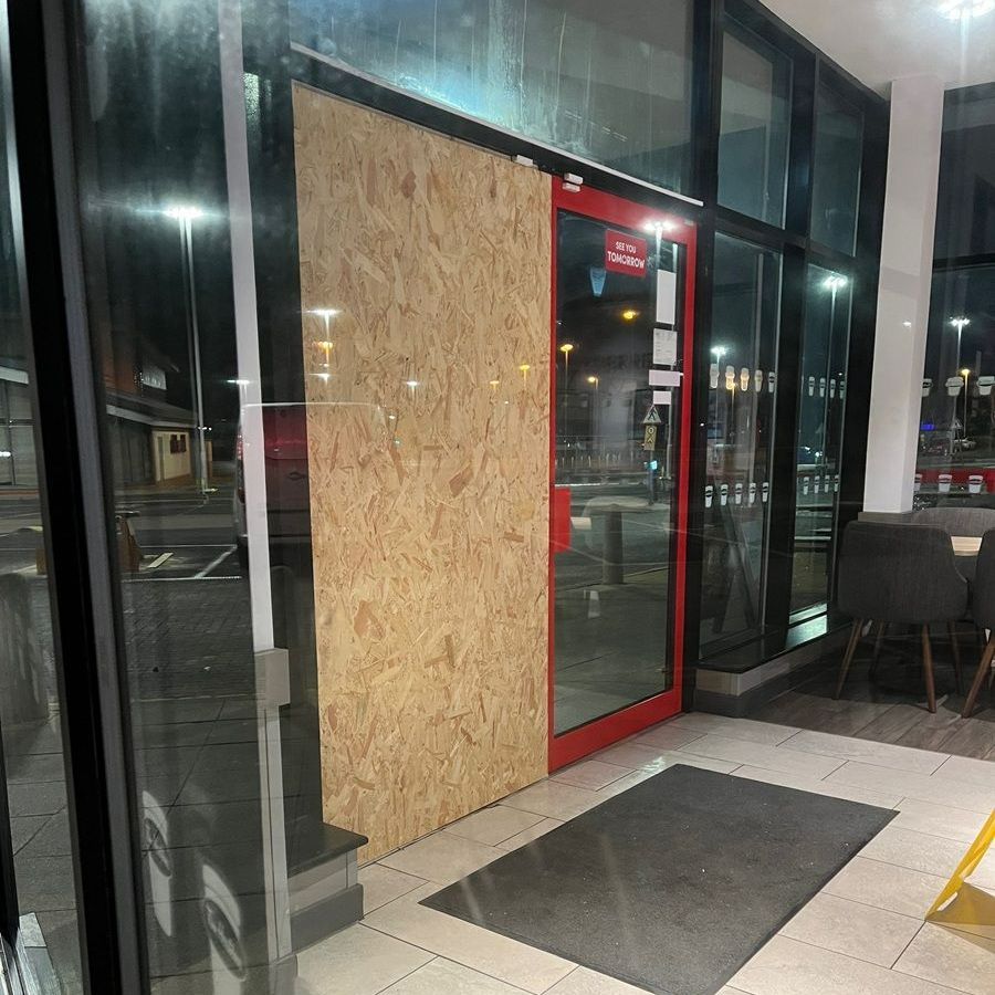 Door boarded up with plywood, inside restaurant. Red door frame, night setting.