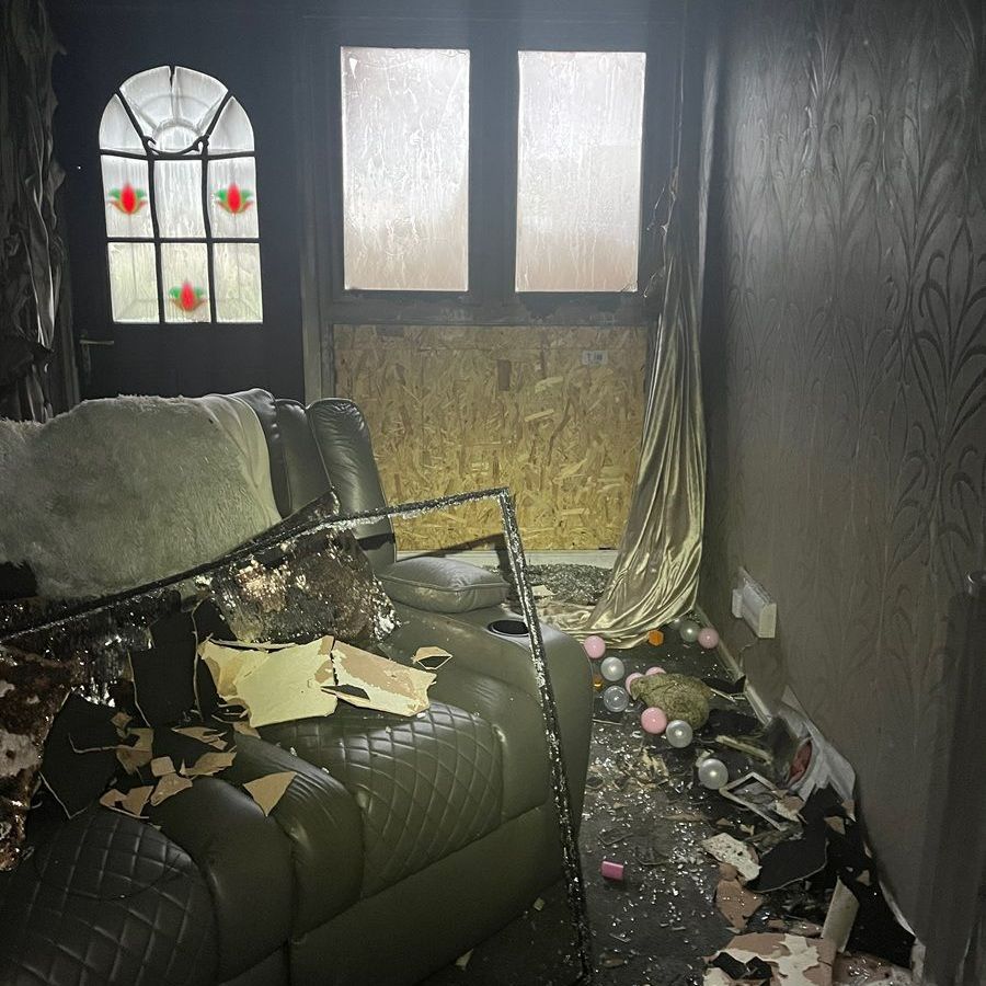 Interior room damaged by fire with a broken window, sofa, and debris.