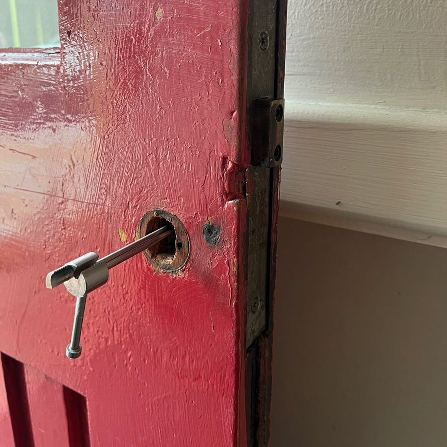 Red door with a tool inserted into the doorknob opening. The door is next to a white wall.
