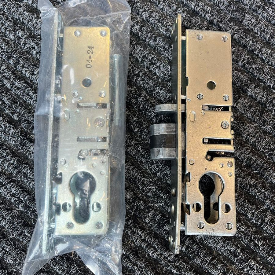 Two silver door lock mechanisms on a dark textured surface; one in plastic packaging.
