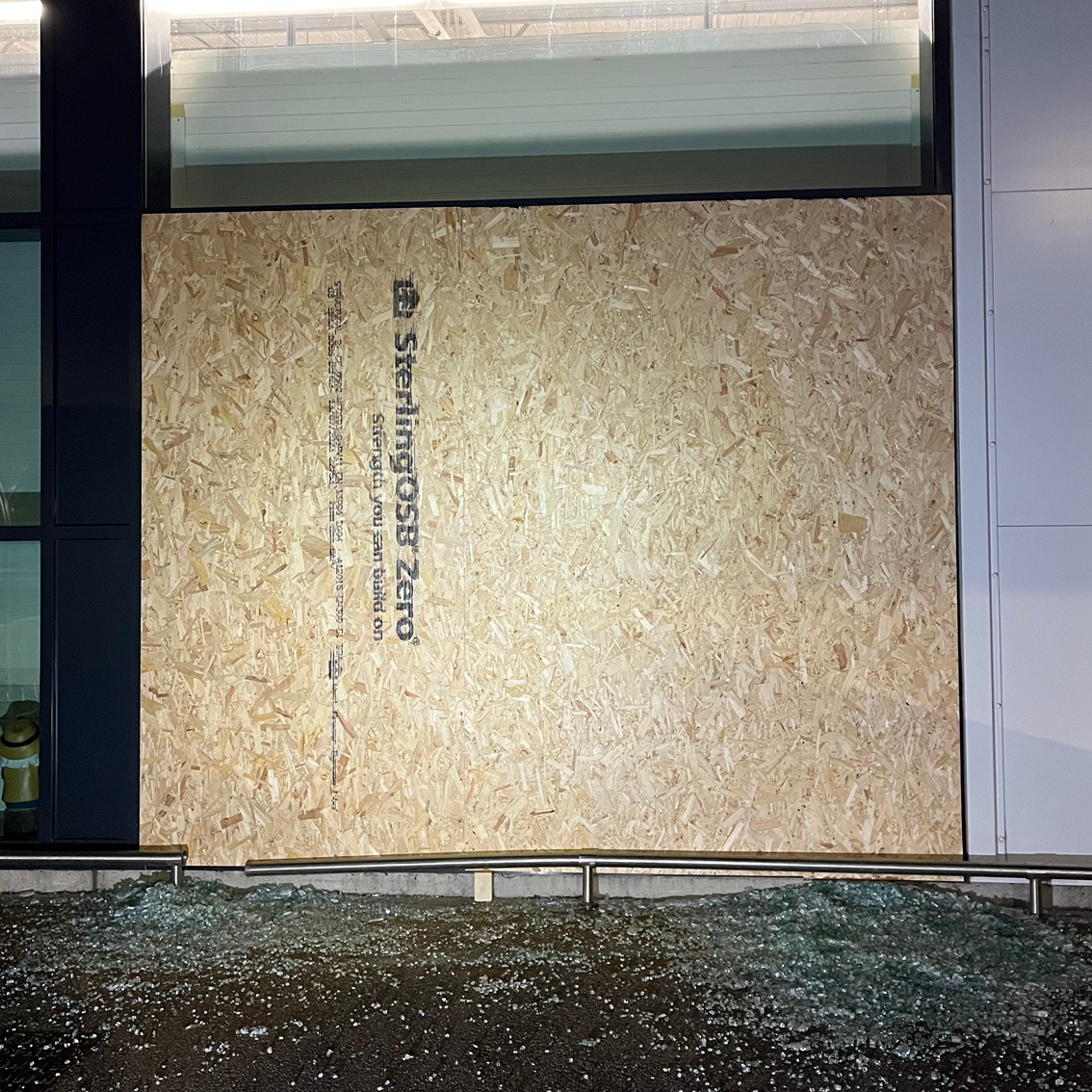 Plywood covers a broken window. Debris litters the ground.