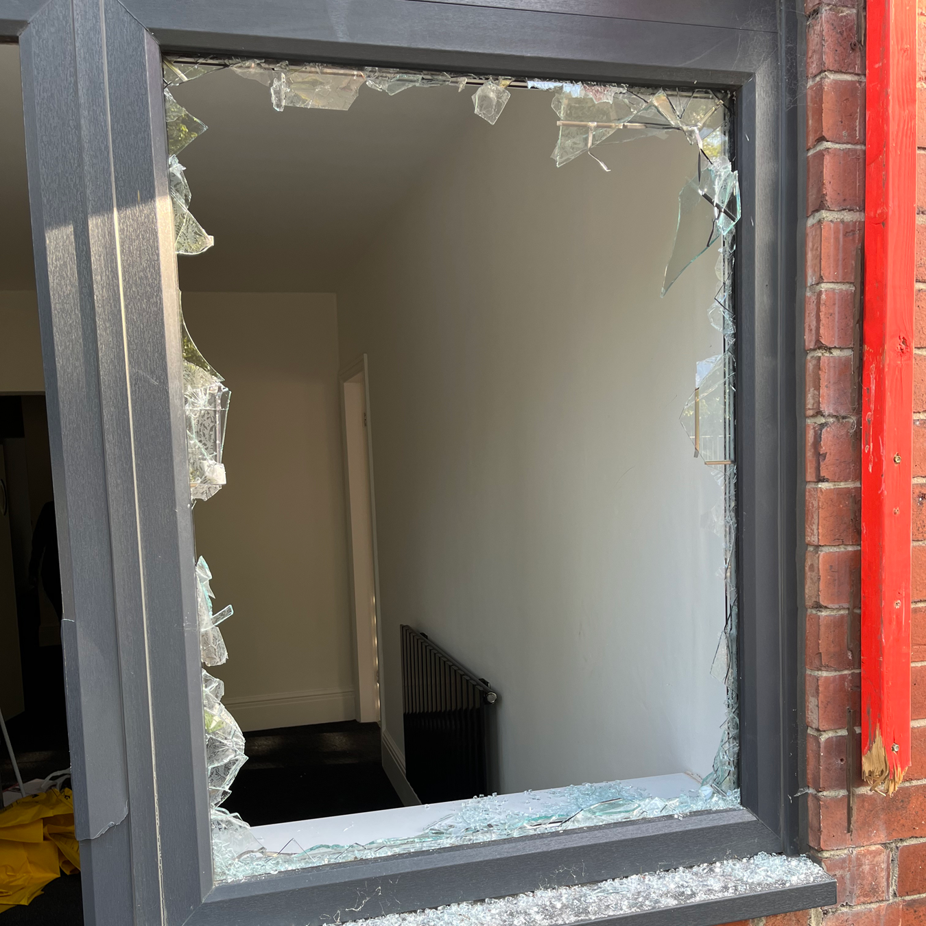 Broken window with shattered glass. Interior hallway visible. Brick exterior.