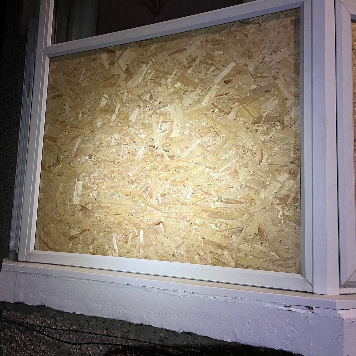 A window with white frame is boarded up with light-colored wood, likely protecting against damage.