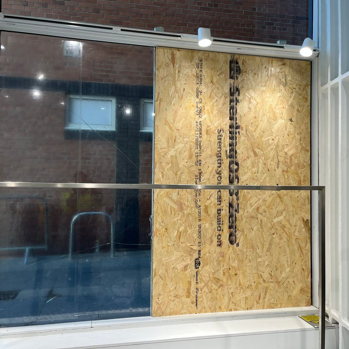 Storefront window, partially boarded up with wood. The left side is glass, the right side is plywood.