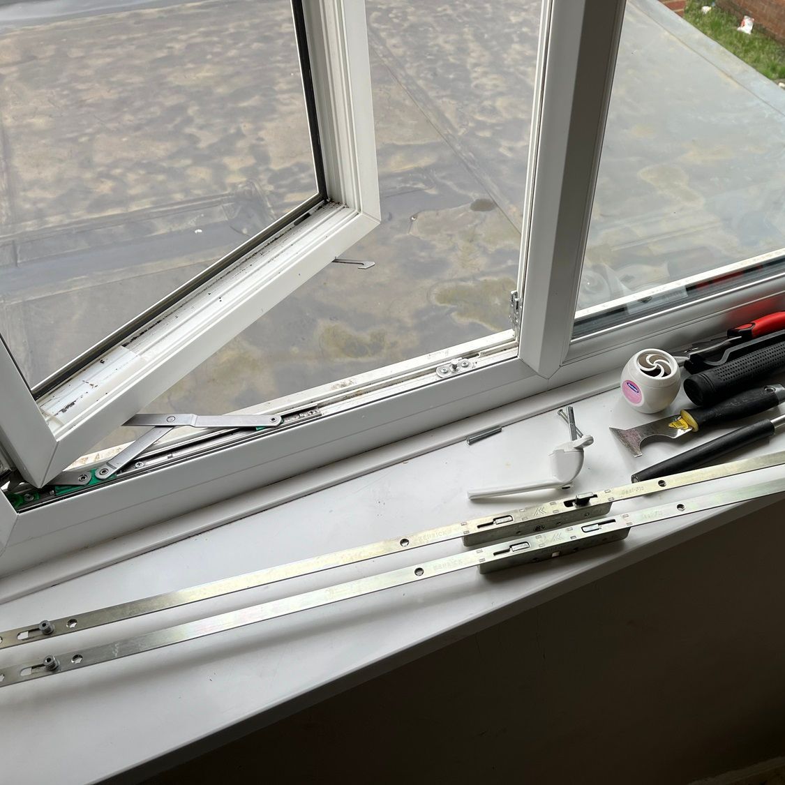 Open white window with hardware on the sill, tools present, suggesting repair or replacement.