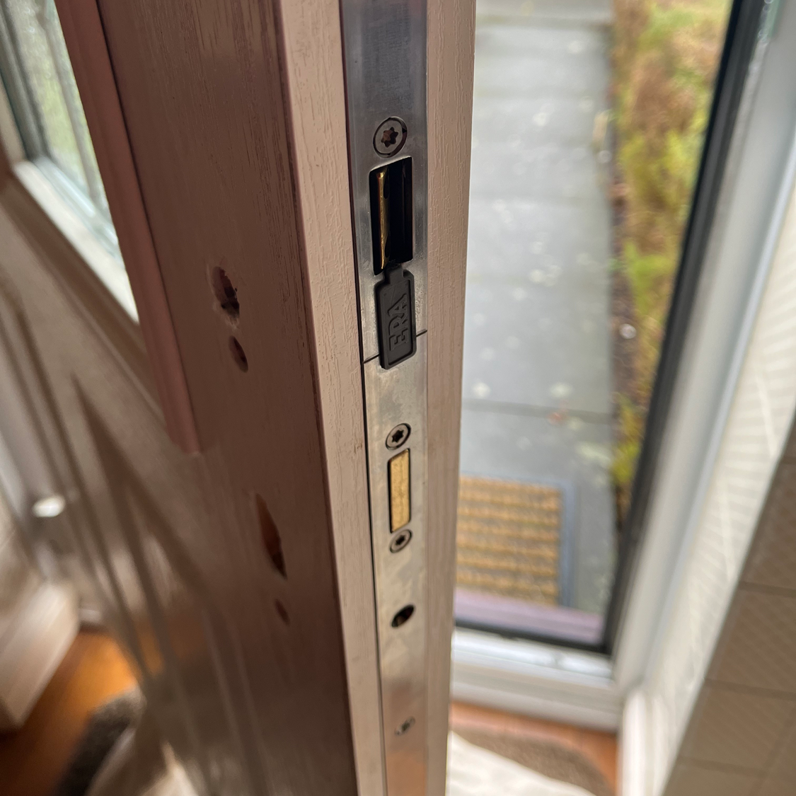 Close-up of a door frame with a lock, and the door's edge; a window is in the background.