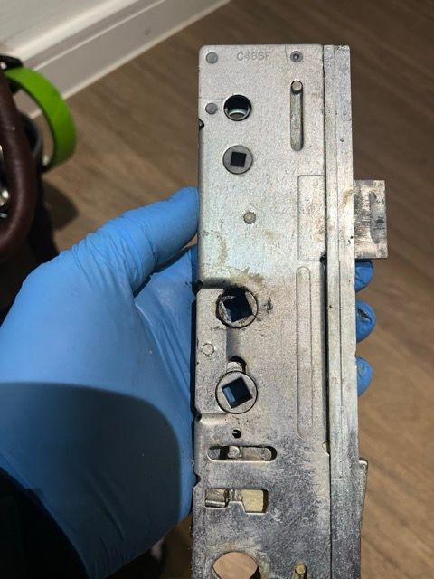 Gloved hand holding a metal door lock mechanism close-up on a wooden floor