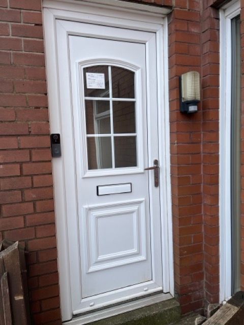 White front door with window panes set in a red brick wall