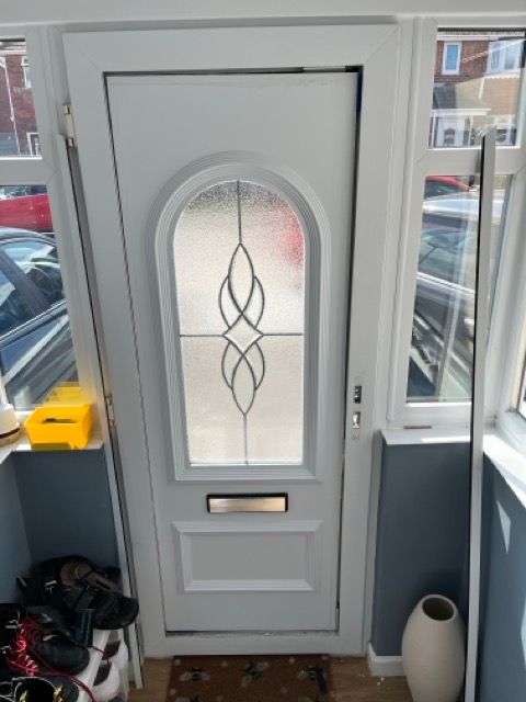 Front door with frosted oval glass panel and black decorative design, seen from inside a small entryway.